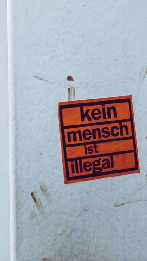 Sobre Nosotros Close-up of a sticker with 'kein mensch ist illegal' on an urban street corner.