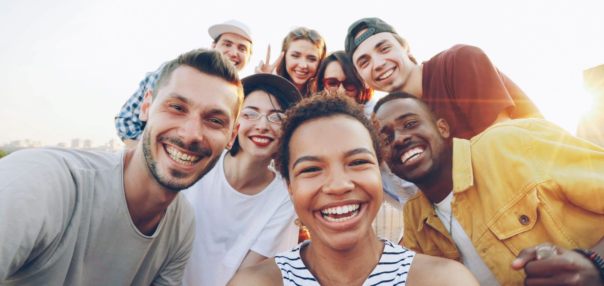 hero-img-01 A diverse group of friends taking a joyful selfie outdoors during sunset.