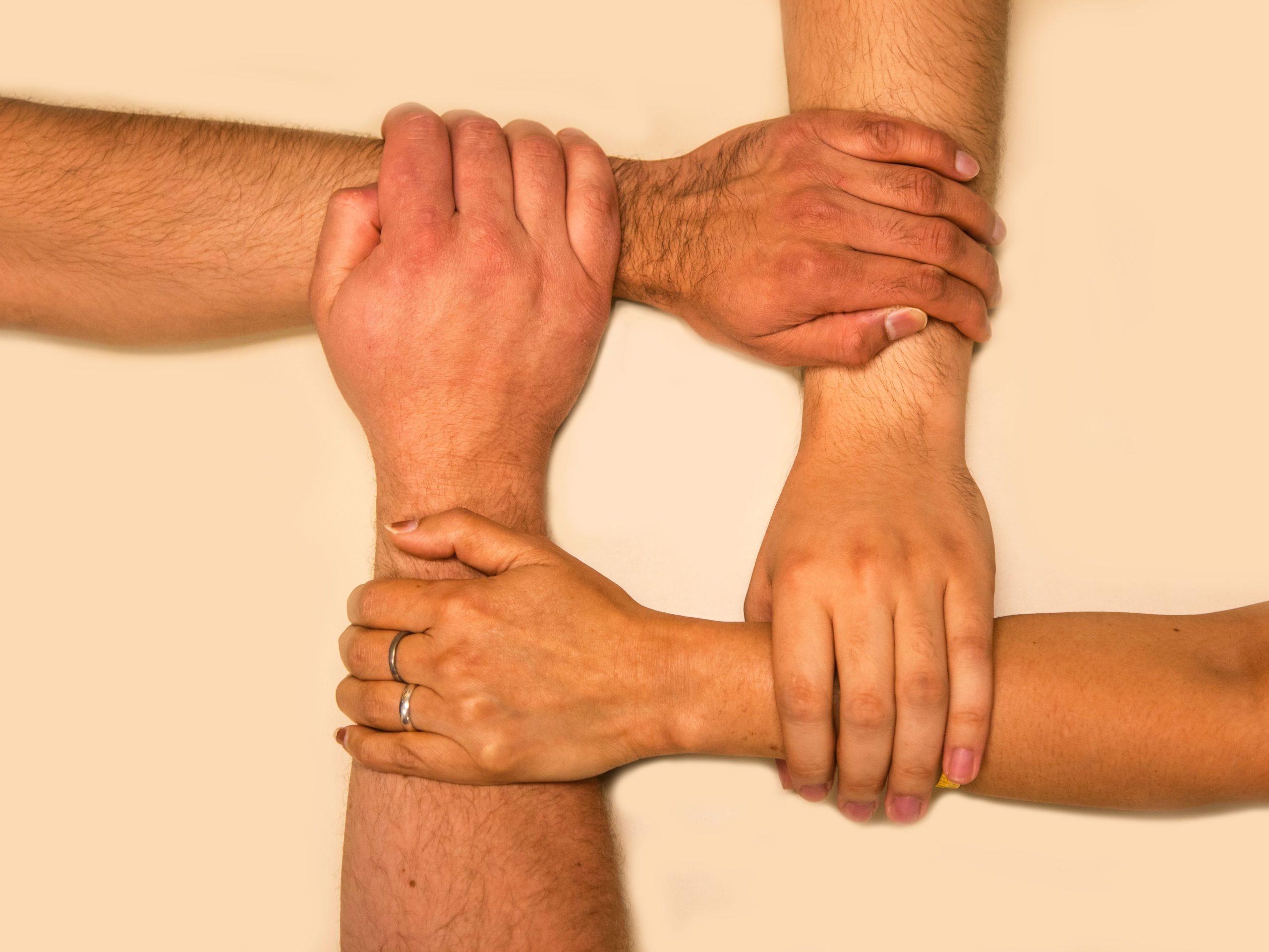 our-services-1 Four hands interlocked, representing unity and teamwork in a symbolic gesture.